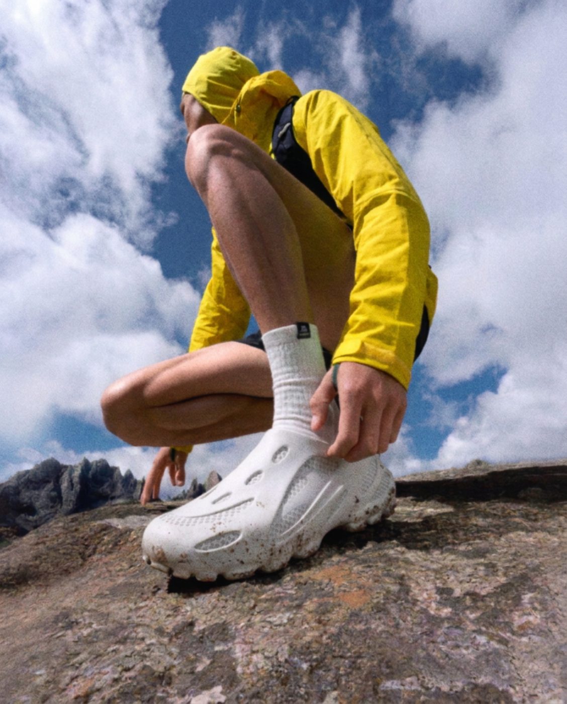 A runner in a yellow jacket pulling on the white Autrion Explorer on a mountain rock.
