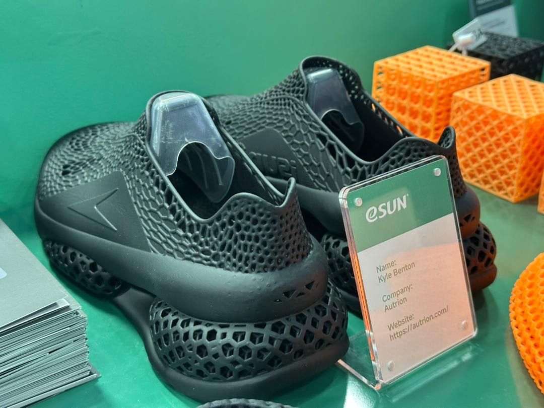 A pair of black printed lattice shoes on the eSUN stand, beside a placard naming Kyle Benton and Autrion.