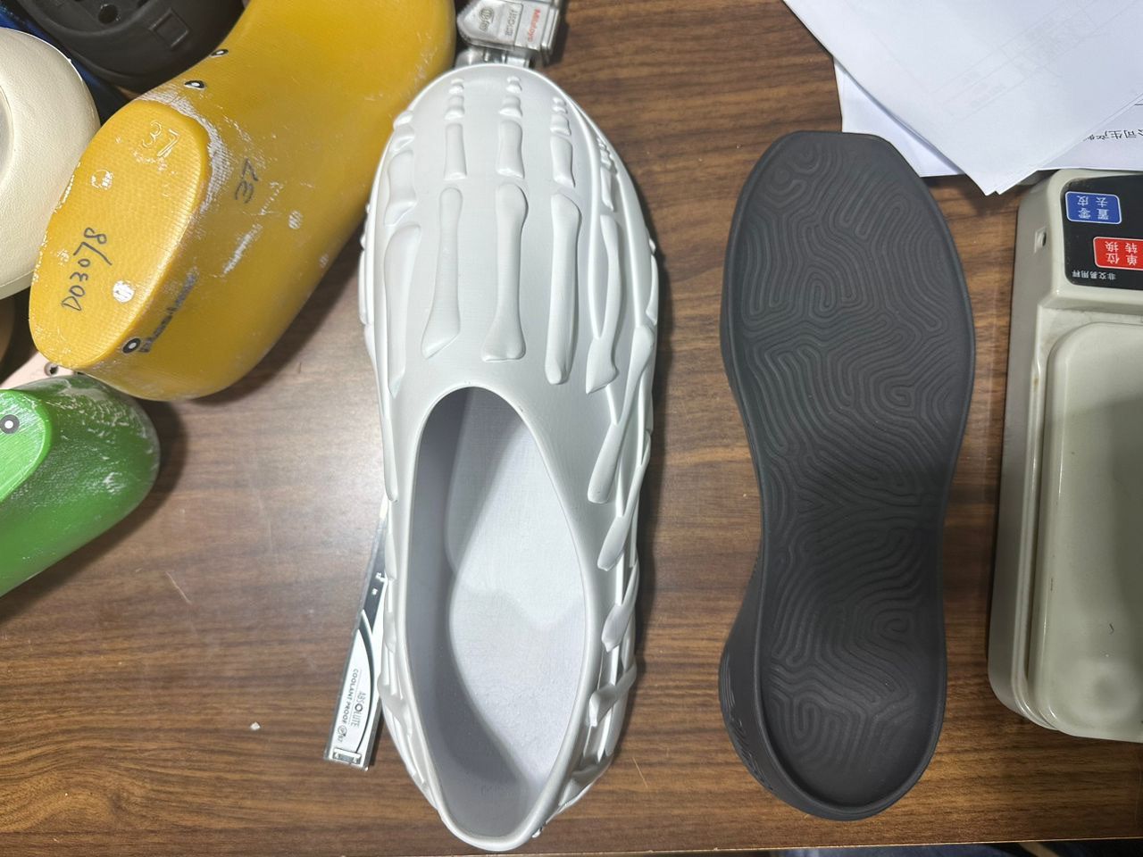 A white molded Gnarcotics clog sample beside an outsole and shoe lasts on a factory desk.